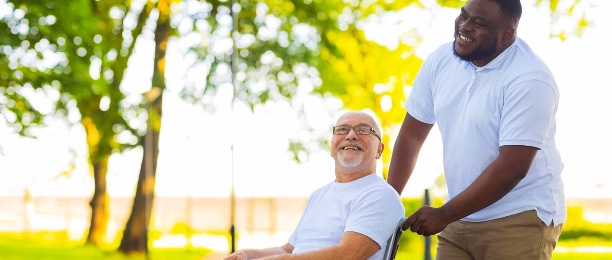 Caregiver and old man in a wheelchair. Professional nurse and patient walking outdoor in the park at sunset. Assistance, rehabilitation and health care concept.
